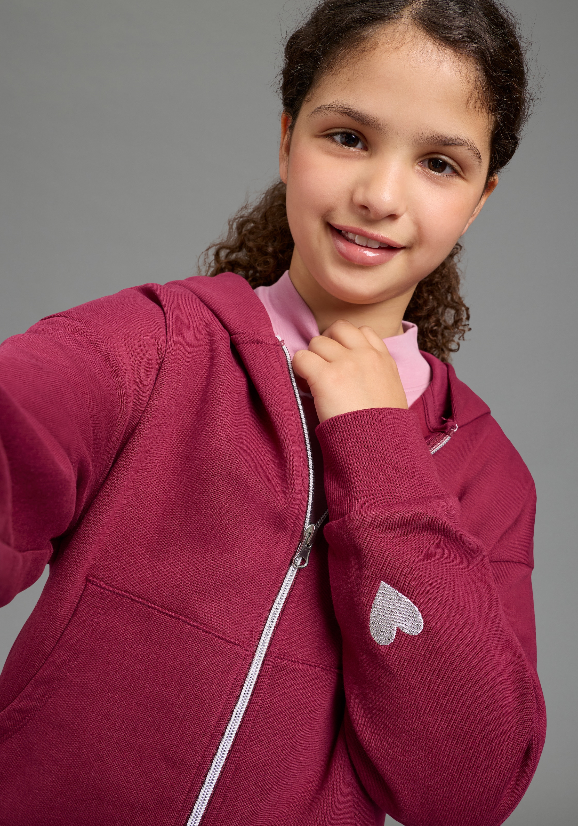 KIDSWORLD Kapuzensweatjacke »Lässige Sweatjacke mit kleinem Herz-Stickerei am Ärmel« Must-Have Basic Sweatjacke mit kleiner Deko-Stickerei, lockere Form